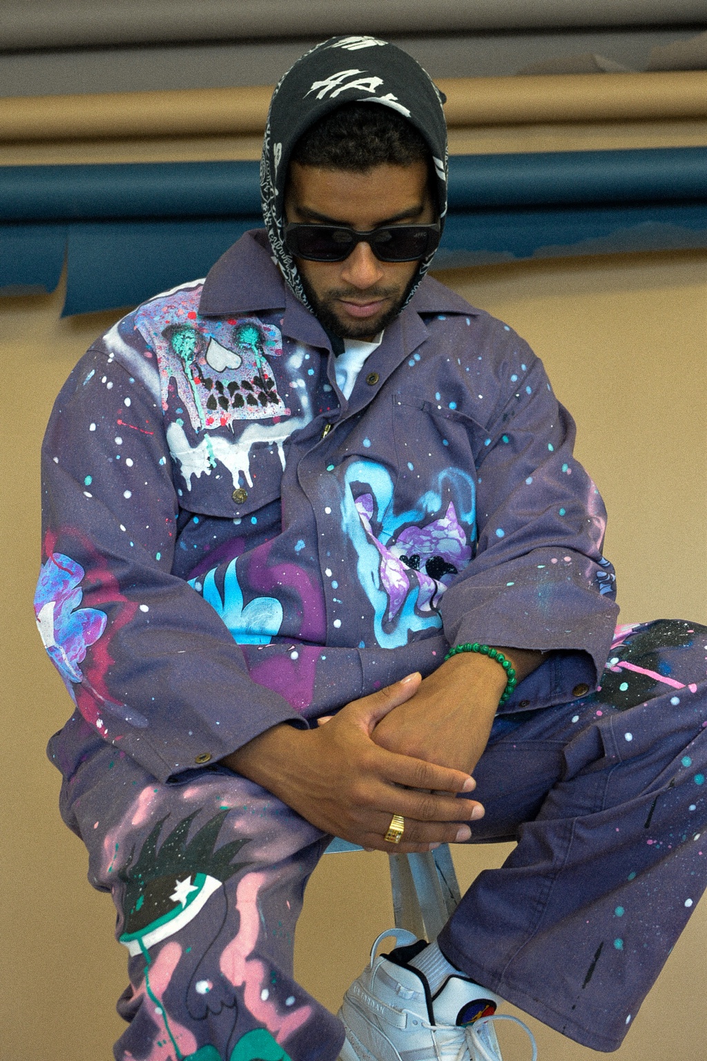 APXO seated wearing the purple hand-painted XCYR boiler suit and sunglasses