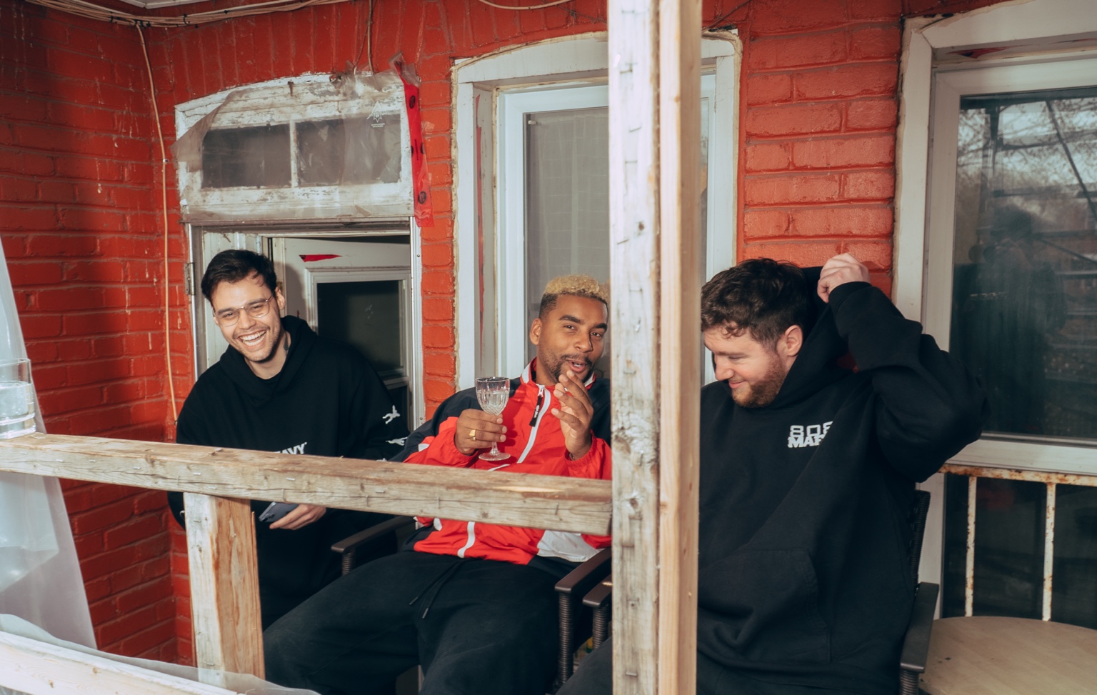 APXO on a balcony with Avian and 808vybz, glass in hand