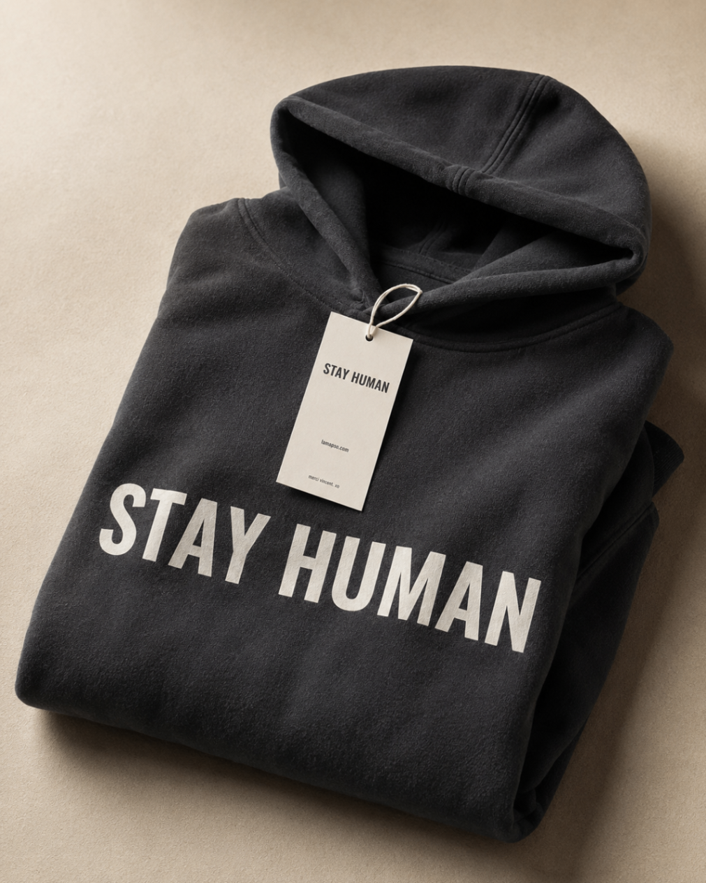 The APXO Stay Human Heavyweight Hoodie folded with the physical hangtag visible, black with cream print.