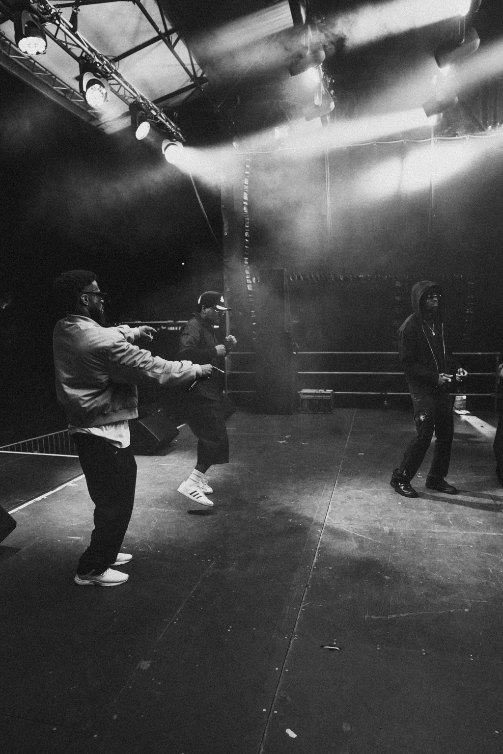 Black and white photograph of three figures on stage during soundcheck under bright lights