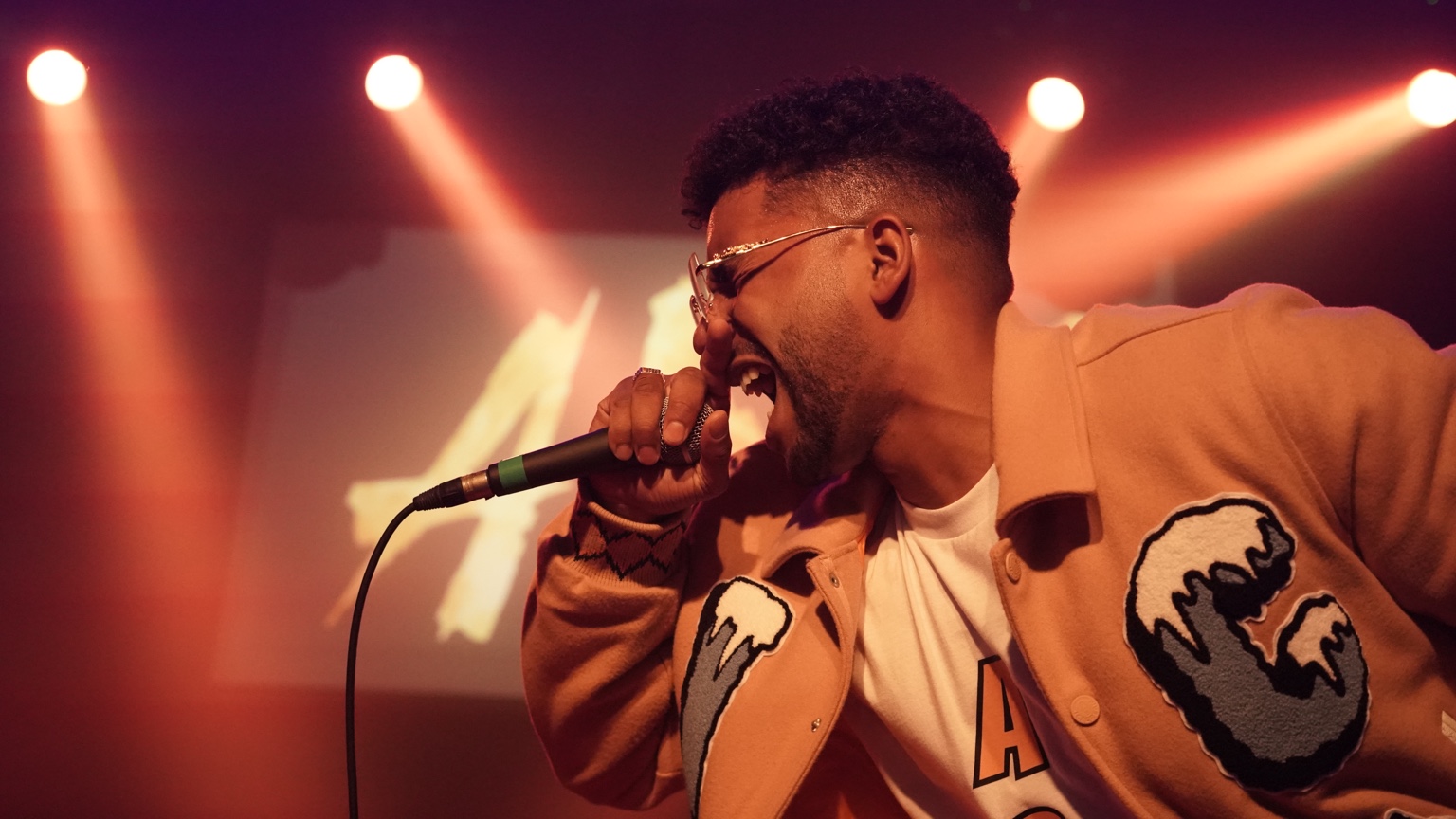 APXO performing under red stage lights in a tan varsity jacket