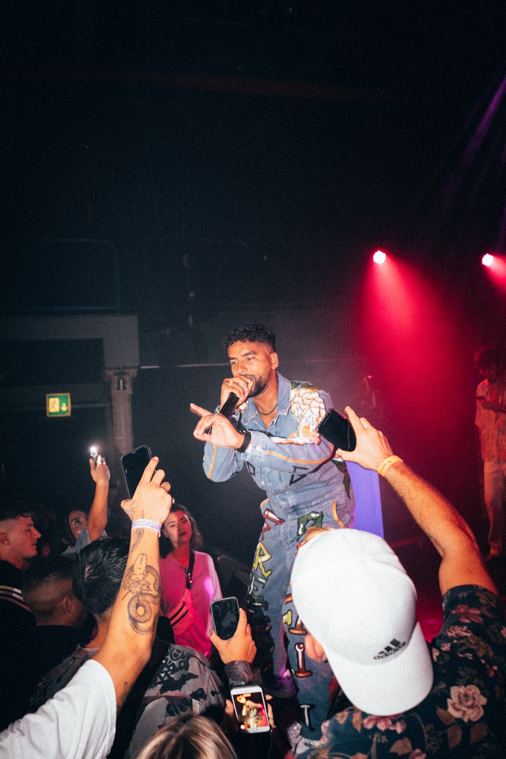 APXO performing on stage in a denim jacket while the audience films on phones