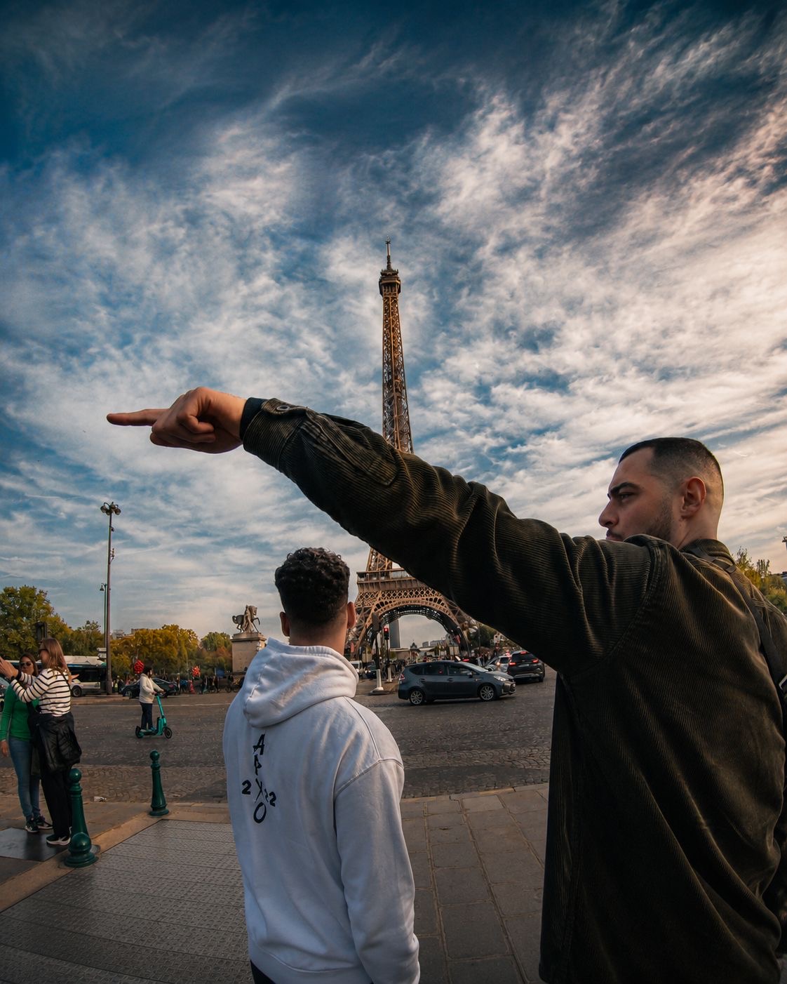 APXO in a green jacket pointing towards the Eiffel Tower under a cloudy sky