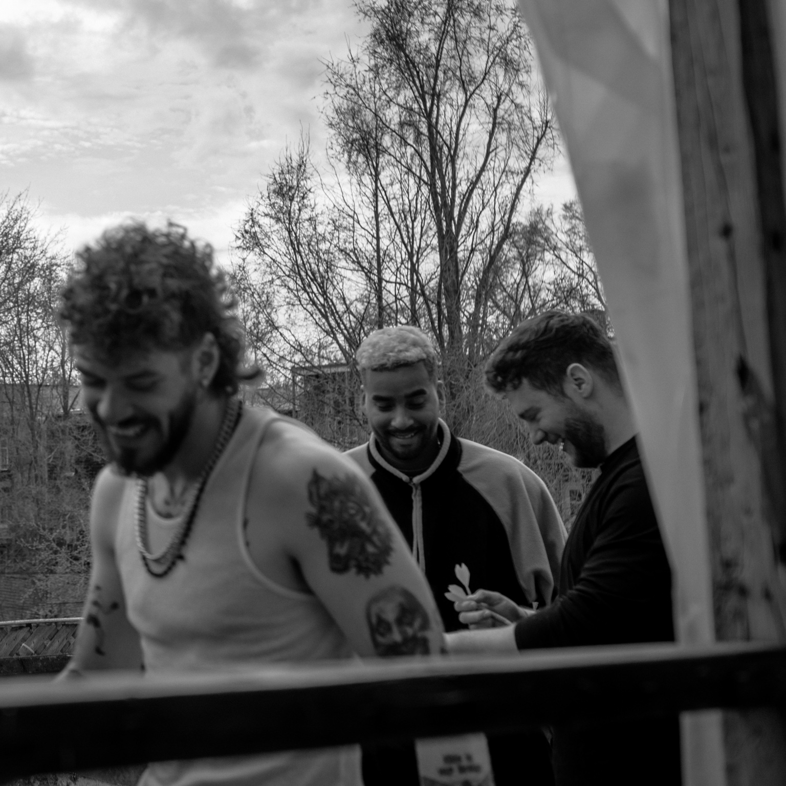Black and white candid photograph of APXO laughing outdoors with his creative circle